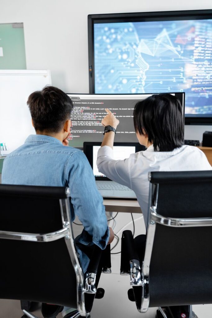 pexels photo 7988759 Two adults collaborating in an office, discussing code on a computer screen.